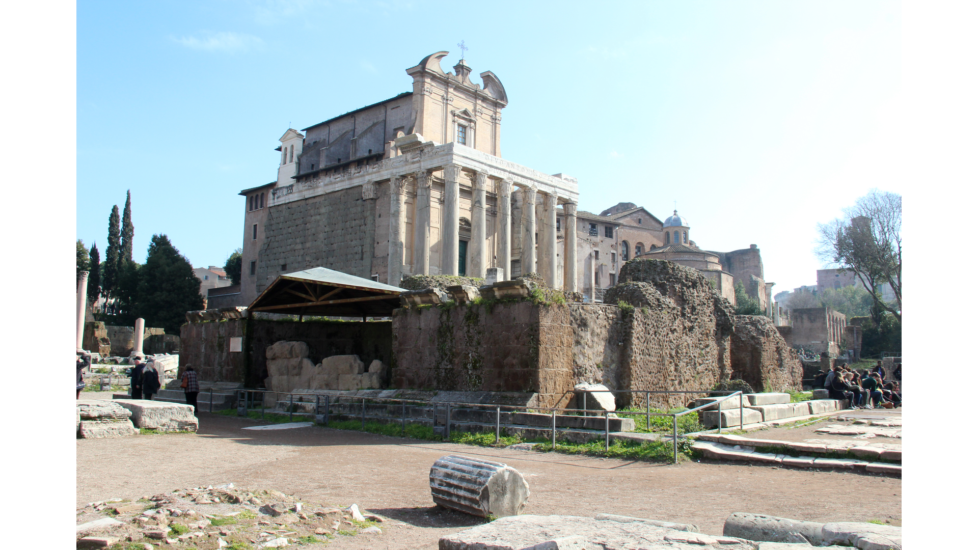 TempleCesarDivinise : Photo prise à Rome aujourd'hui. Vestiges du podium du temple de César divinisé avec le temple d’Antonin et Faustine en arrière-plan