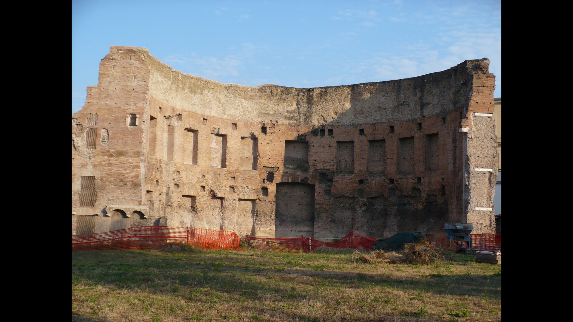 Un grand mur ancien en pierre et brique, partiellement érodé, avec des ouvertures irrégulières et des traces d'usure visible.