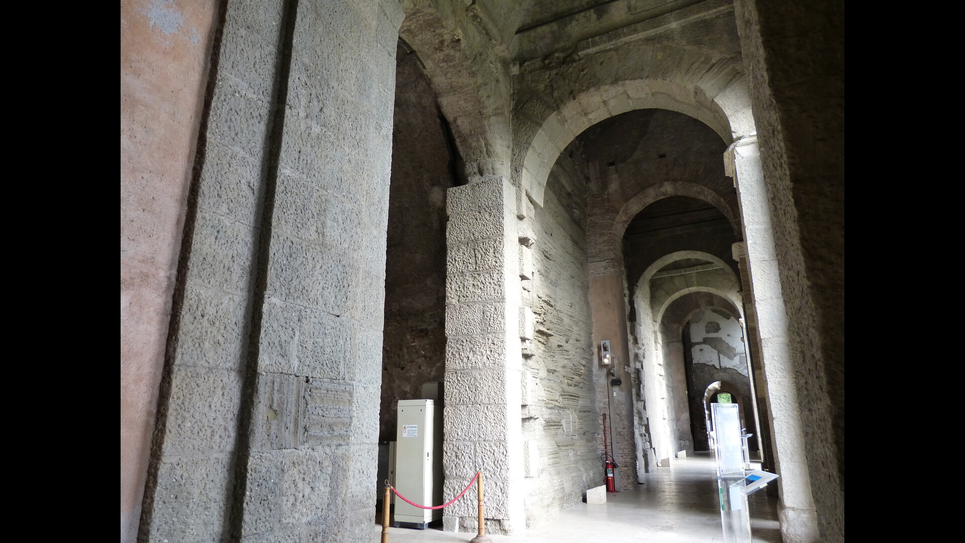 Une série d'arcades en pierre formant une longue galerie voûtée et éclairée par des ouvertures à chaque extrémité.